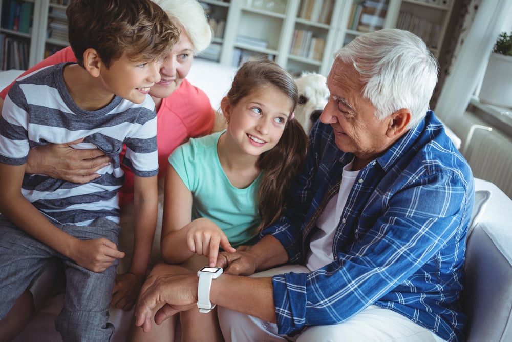 Grandparents and grandchildren looking at smartwatch in living room at home