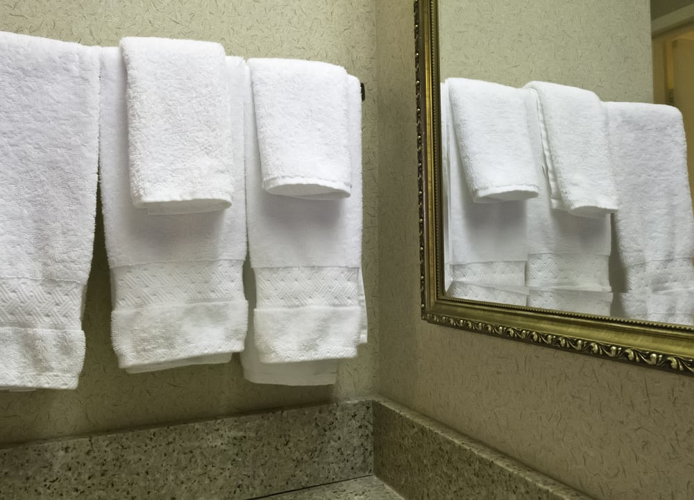 Housekeeping at a glance Five white terrycloth towels reflected by wall mirror in hotel bathroom